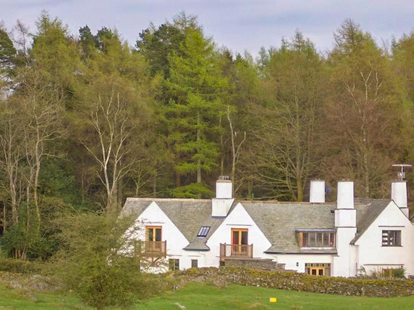 Lickbarrow Lodge, a white Arts and Crafts house with balconies and tall chimneys, set against woodland